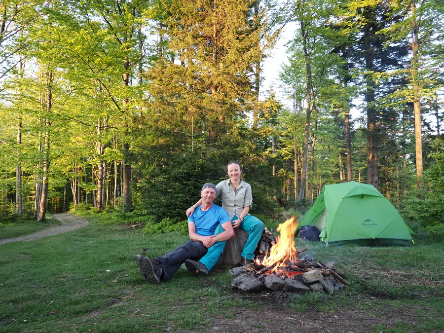 Two travellers beside a campfire and a green tent in a forest.