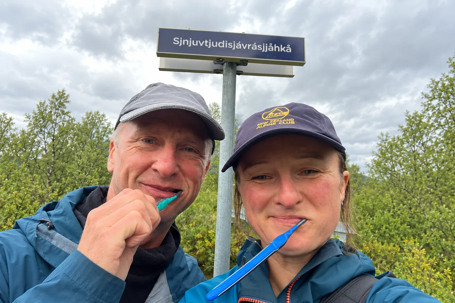 Two travellers brushing their teeth beneath a Sámi place-name sign. Sarek NP, 2026