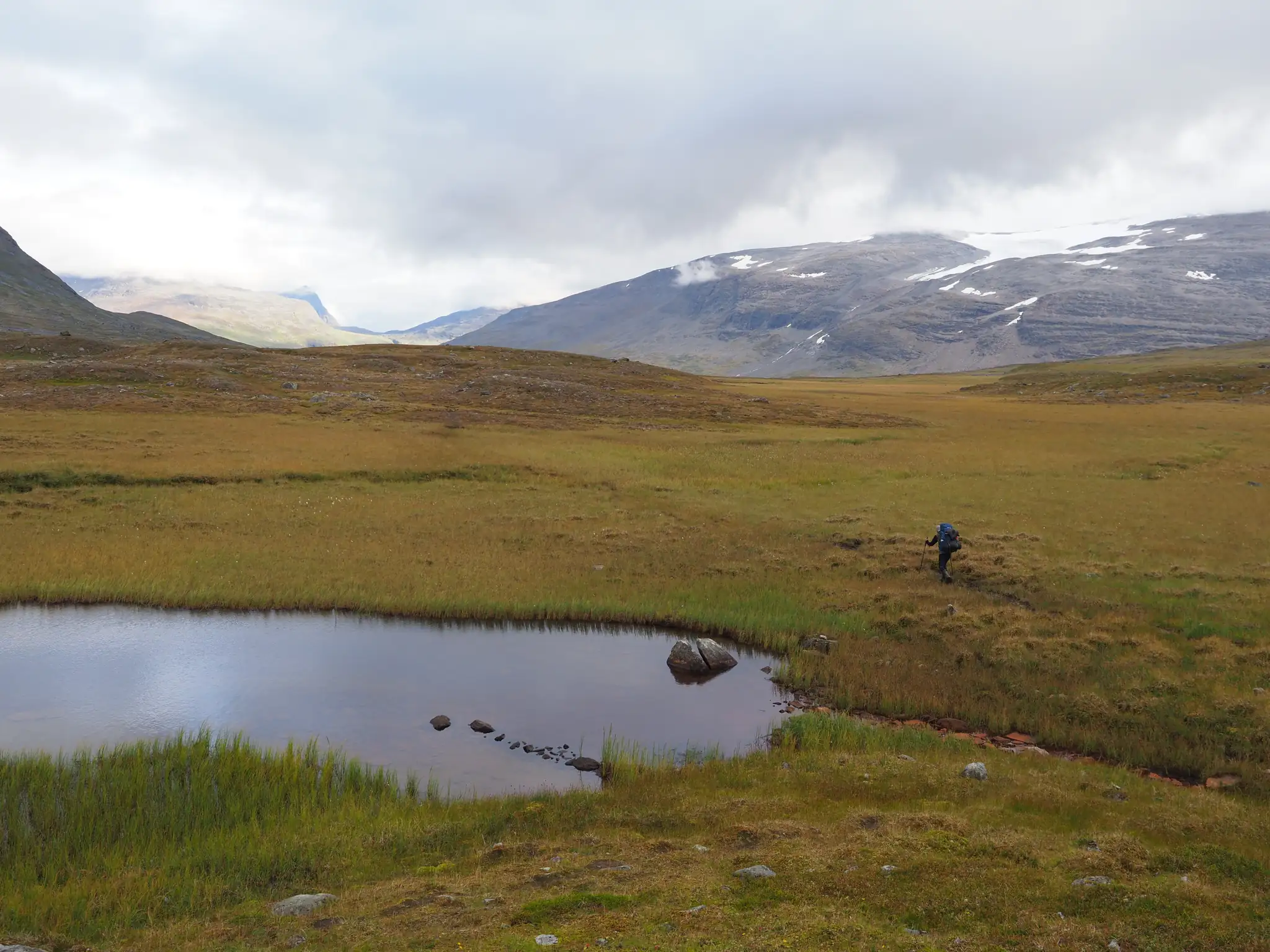 Rafał walking beside a small pond in a mountain valley.