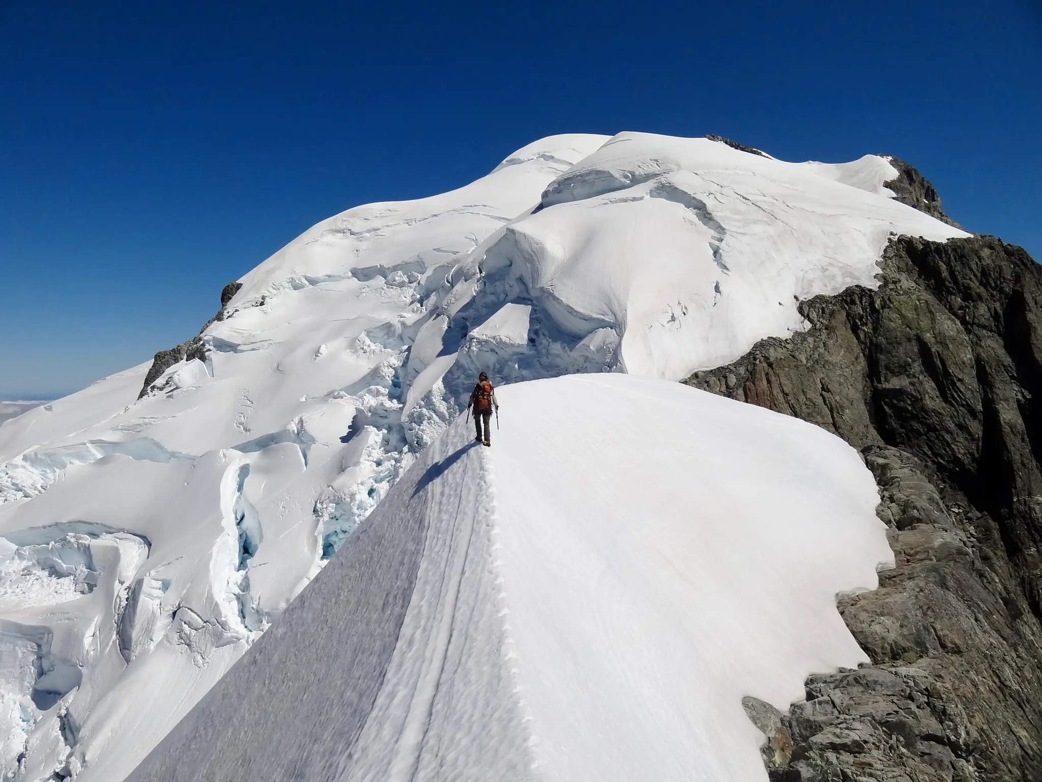 Joanna on the snow ridge of Mount Tutoko, with seracs visible below the summit dome.
