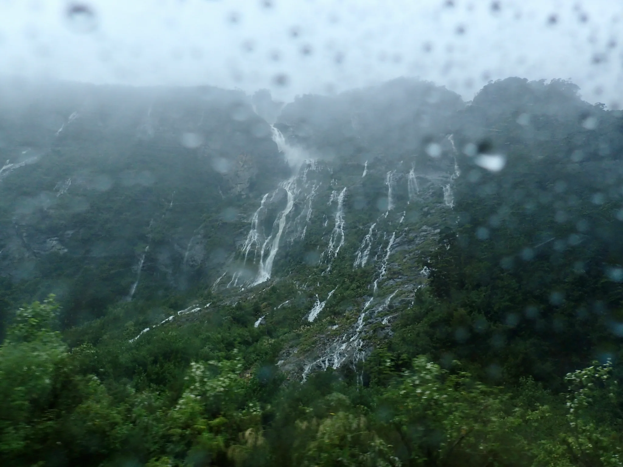 Rain falling over lush hillsides and swollen waterfalls.