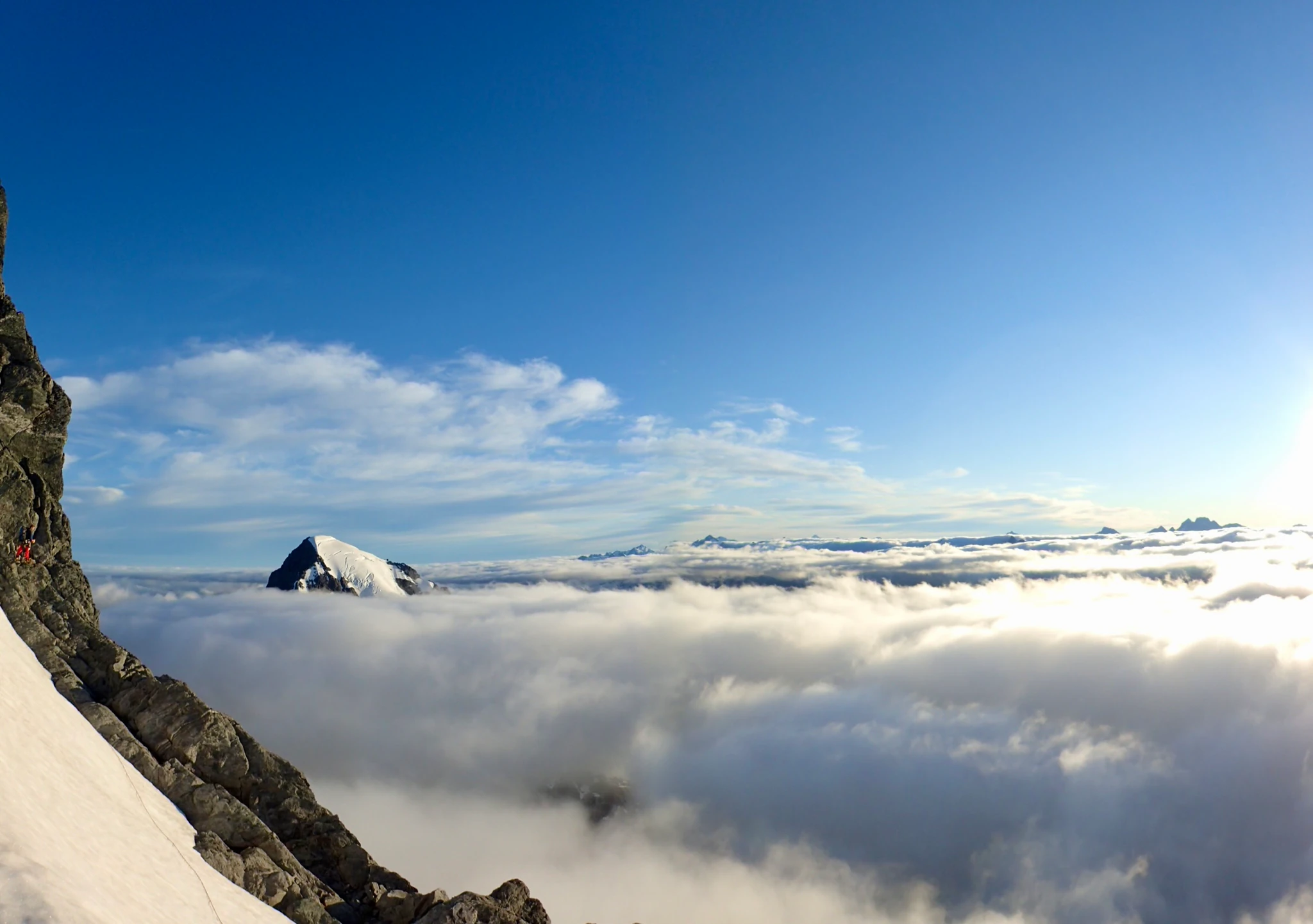 Willie at the base of a rock tower on the far side of Mount Tutoko's ridge, above a sea of clouds.