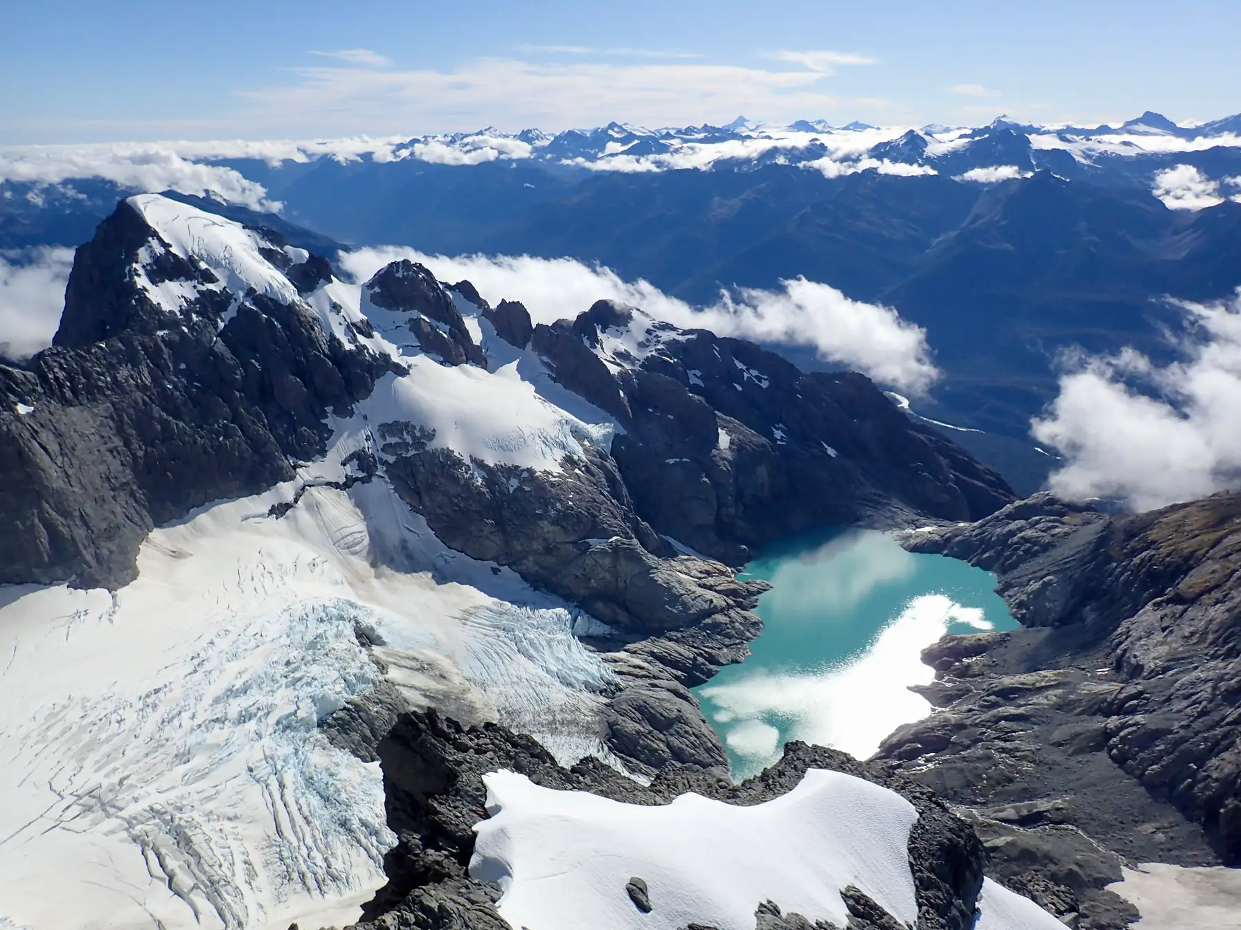 Wide view of a turquoise alpine lake, with surrounding mountains on the horizon.